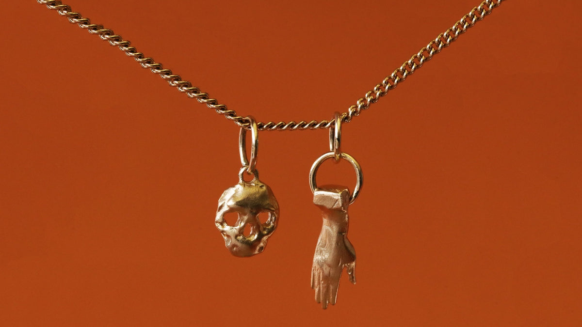 Two yellow gold pendants on a chain by 12th House with an orange backdrop