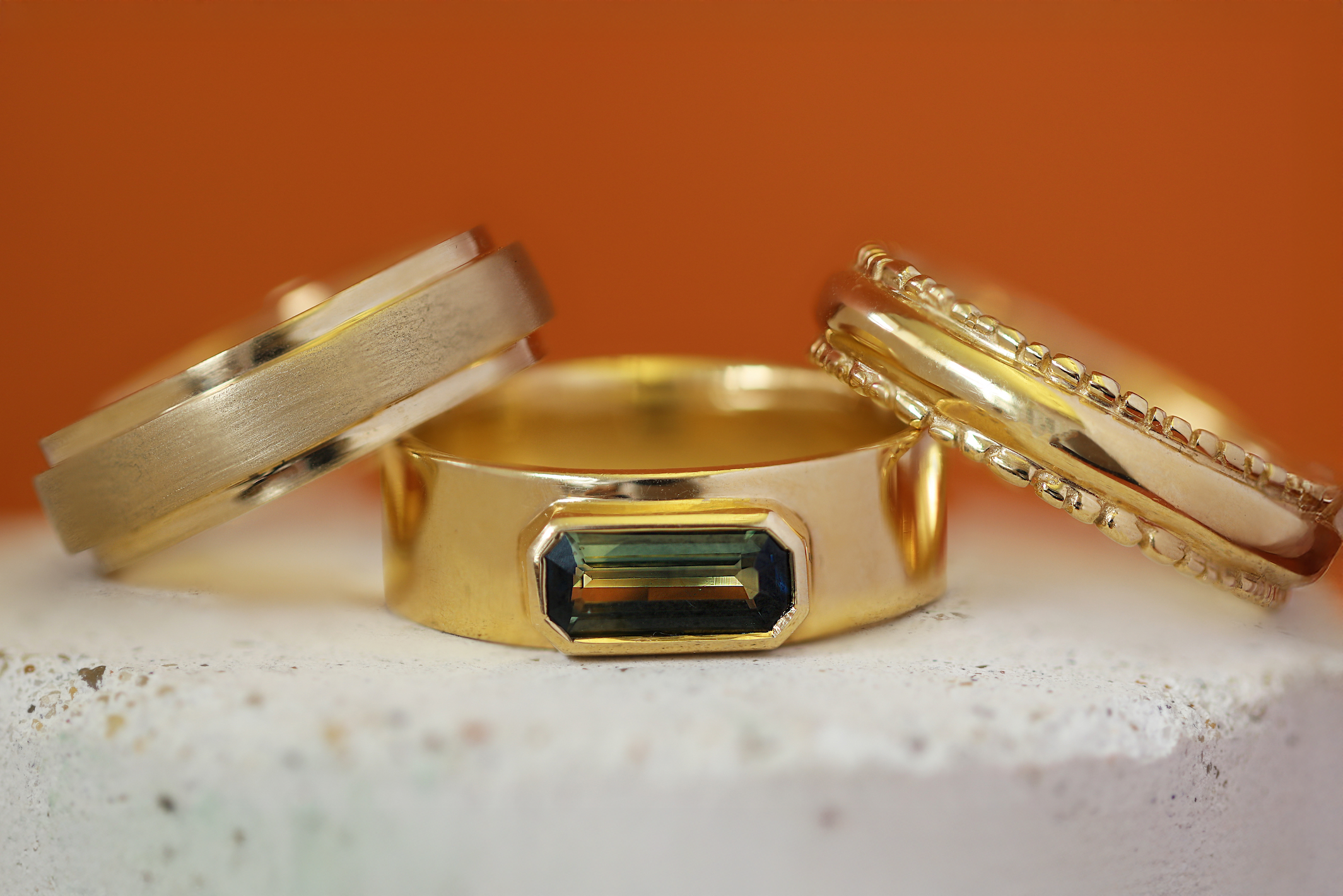 Stacked view of Kingsland Ring Emerald Cut Sapphire 1.2ct, Cornice Band Wide Flat in Yellow Gold, and Ruins Dome Band by Goldpoint