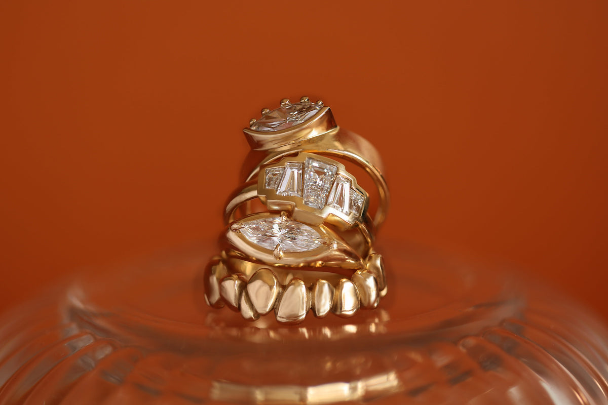 A stack of bold and chunky engagement rings and wedding bands by Goldpoint Jewelry on an orange background