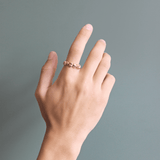 Model wears Ruins Wide Band in 14k yellow gold by Goldpoint Jewelry on index finger with a teal backdrop