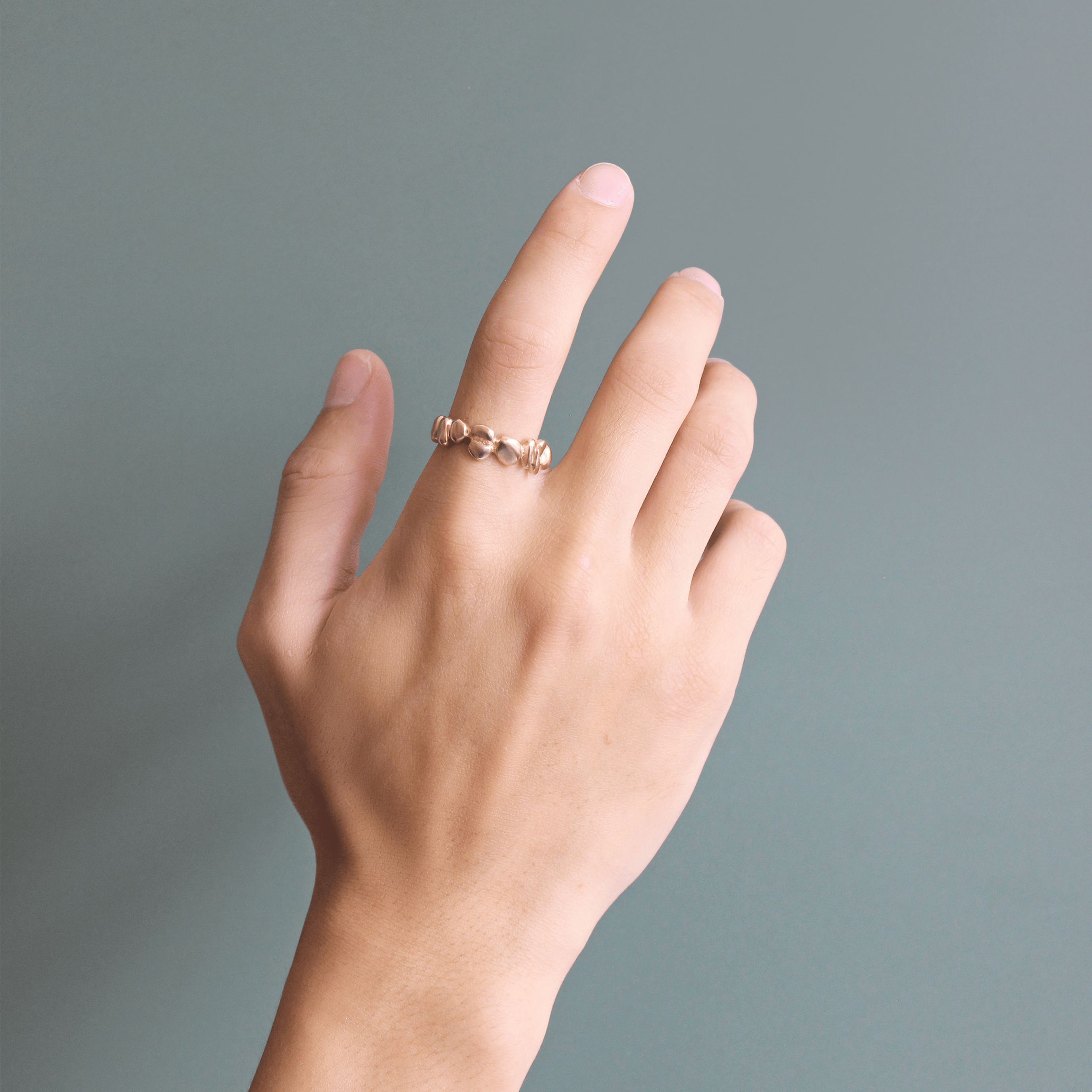 Model wears Ruins Wide Band in 14k yellow gold by Goldpoint Jewelry on index finger with a teal backdrop