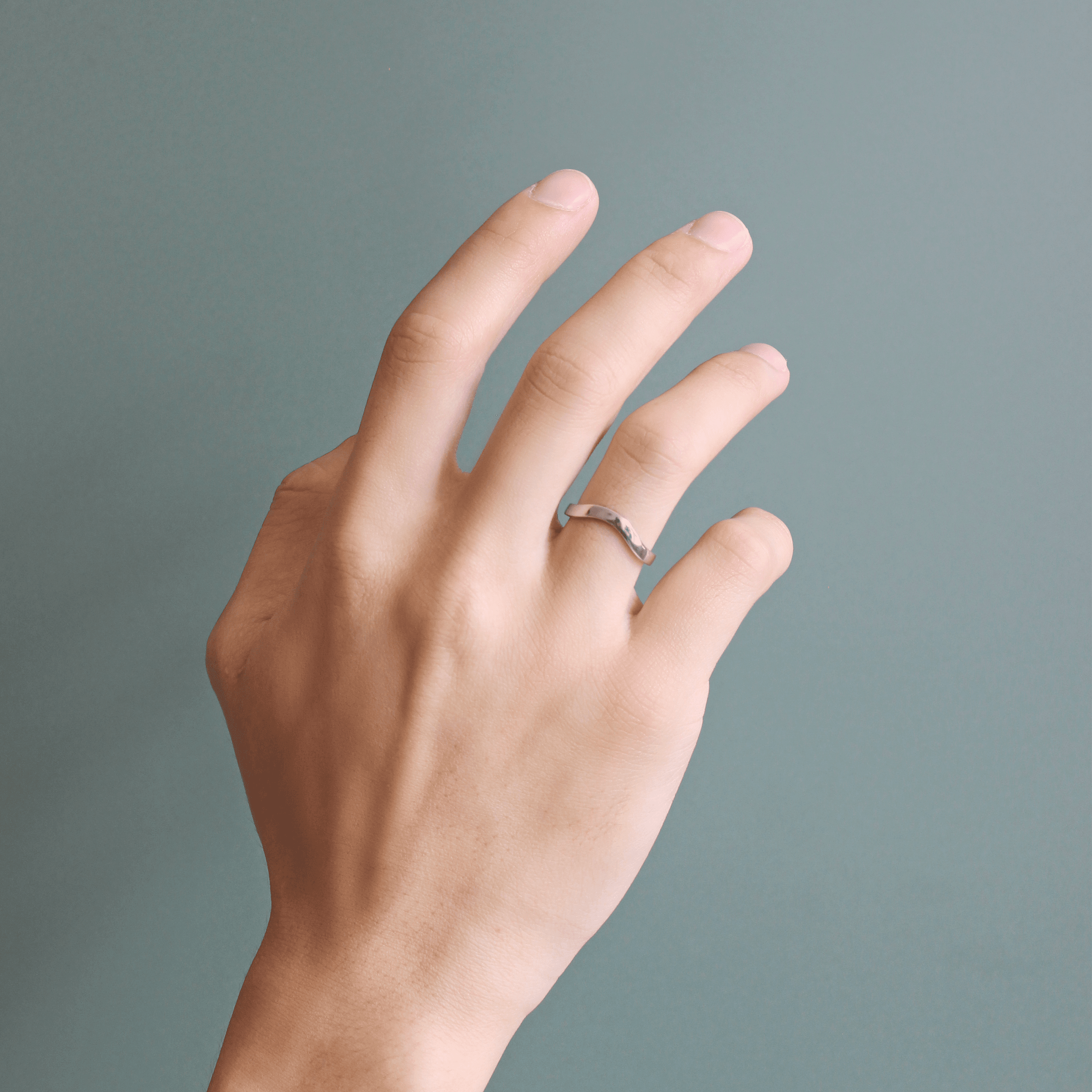 Model wears Flat Wide Band Deep Curve in Platinum by Goldpoint Jewelry on ring finger on teal background