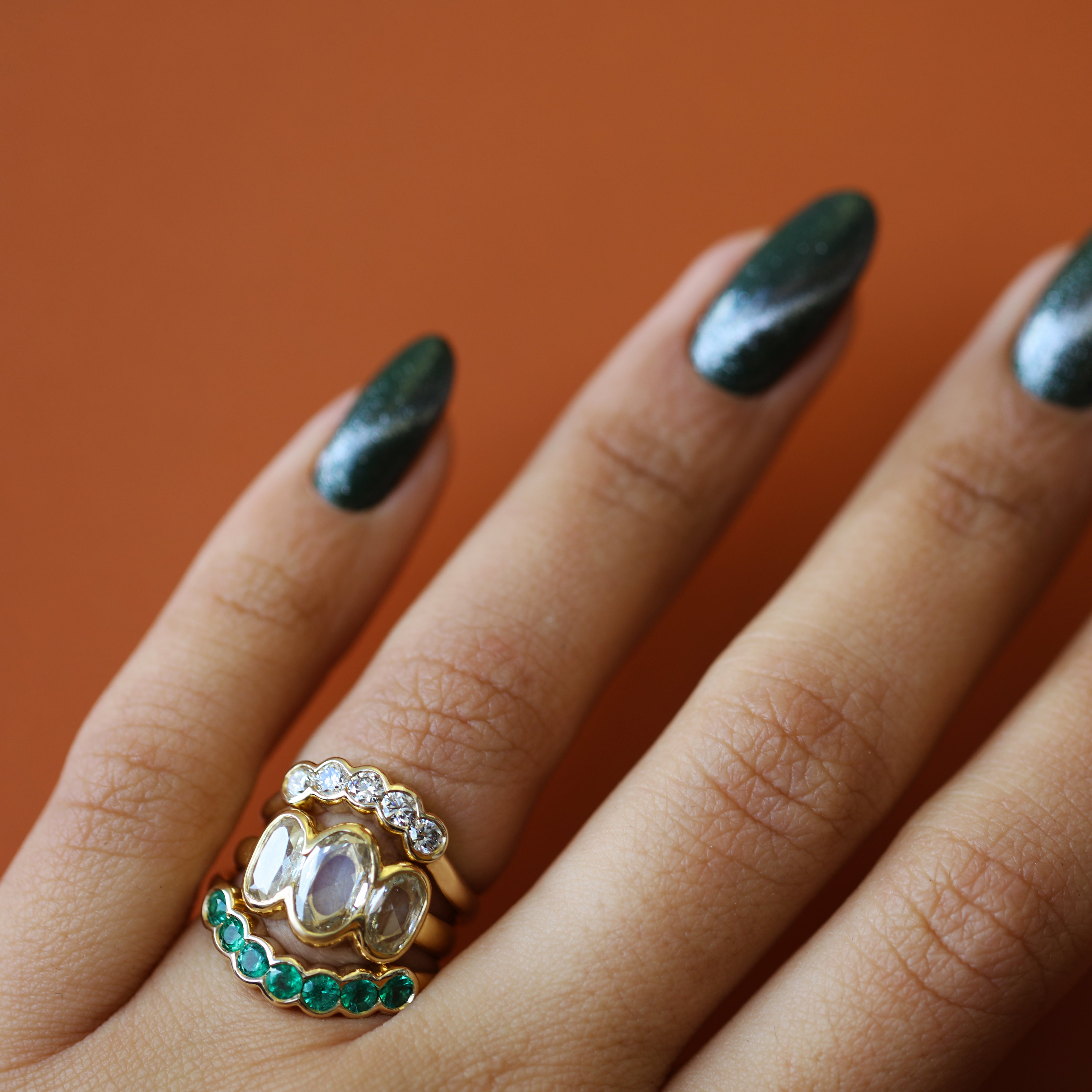 Model wears Cloud 7 Band Curve Round Emeralds in 14k yellow gold, Clay 3 Ring Oval Natural Diamond 1.08ct in 18k yellow gold, and Cloud 5 Band Curve 
Round Lab Diamonds in 14k yellow gold stacked on their ring finger