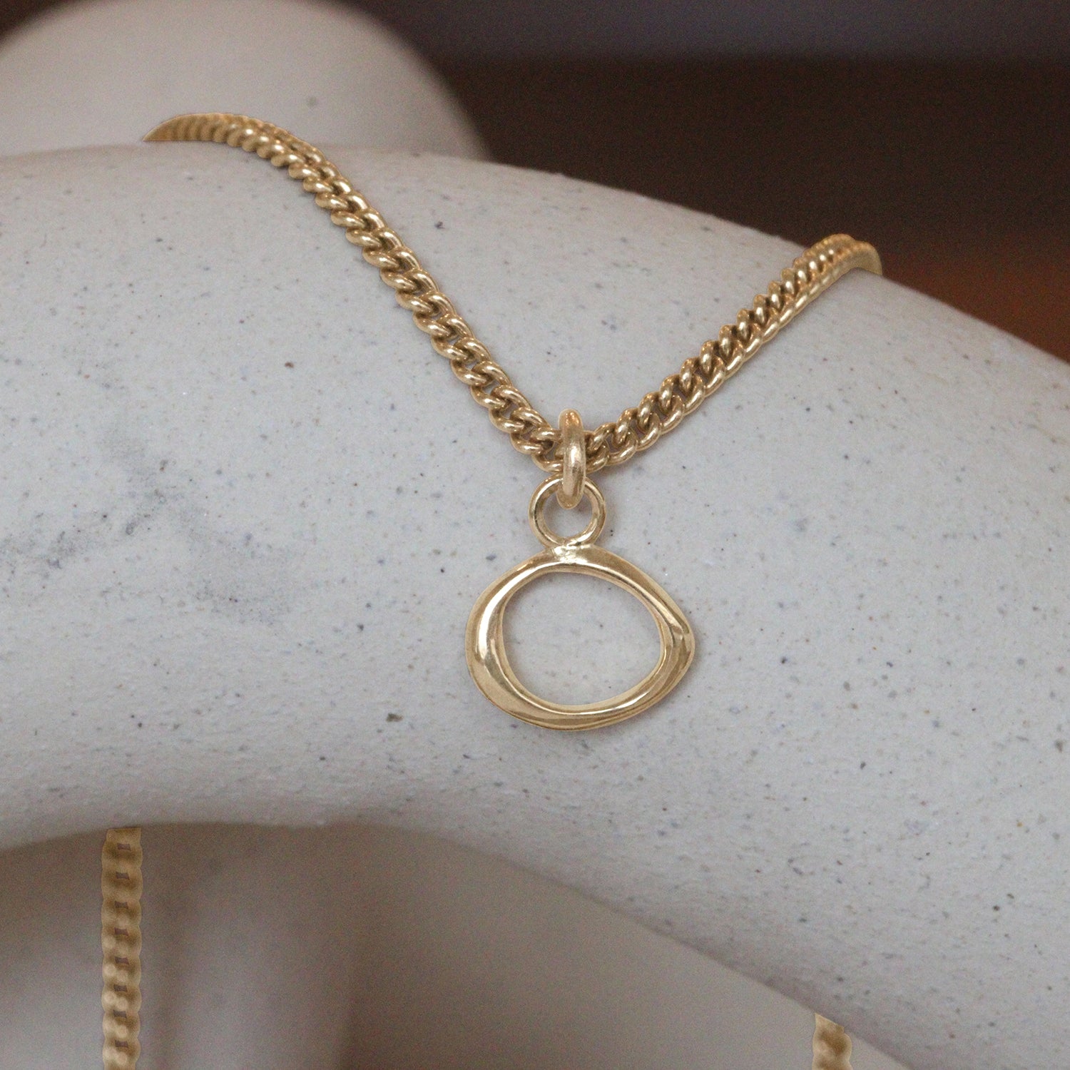 Lifestyle front view of Amorphous Charm / Small Circle on a chain by Goldpoint Jewelry on a ceramic with blurred background
