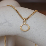 Lifestyle front view of Amorphous Charm / Small Circle on a chain by Goldpoint Jewelry on a ceramic with blurred background