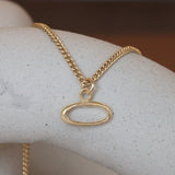 Lifestyle front view of Amorphous Charm / Oval Sideways on a chainby Goldpoint Jewelry sitting on a ceramic with blurred background