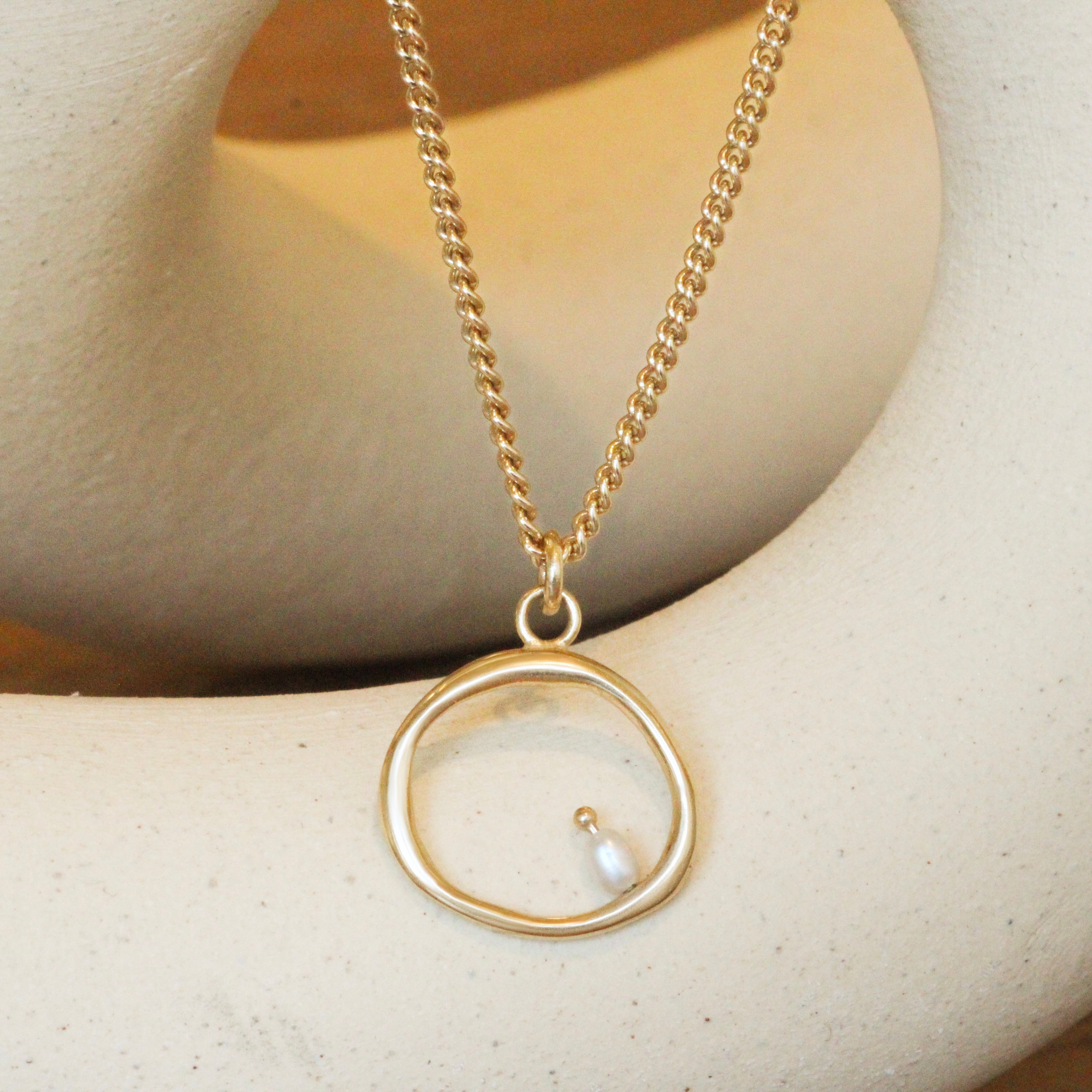 Lifestyle front view of Amorphous Pearl Bead Charm / Large Circle by Goldpoint Jewelry on a chain over a ceramic