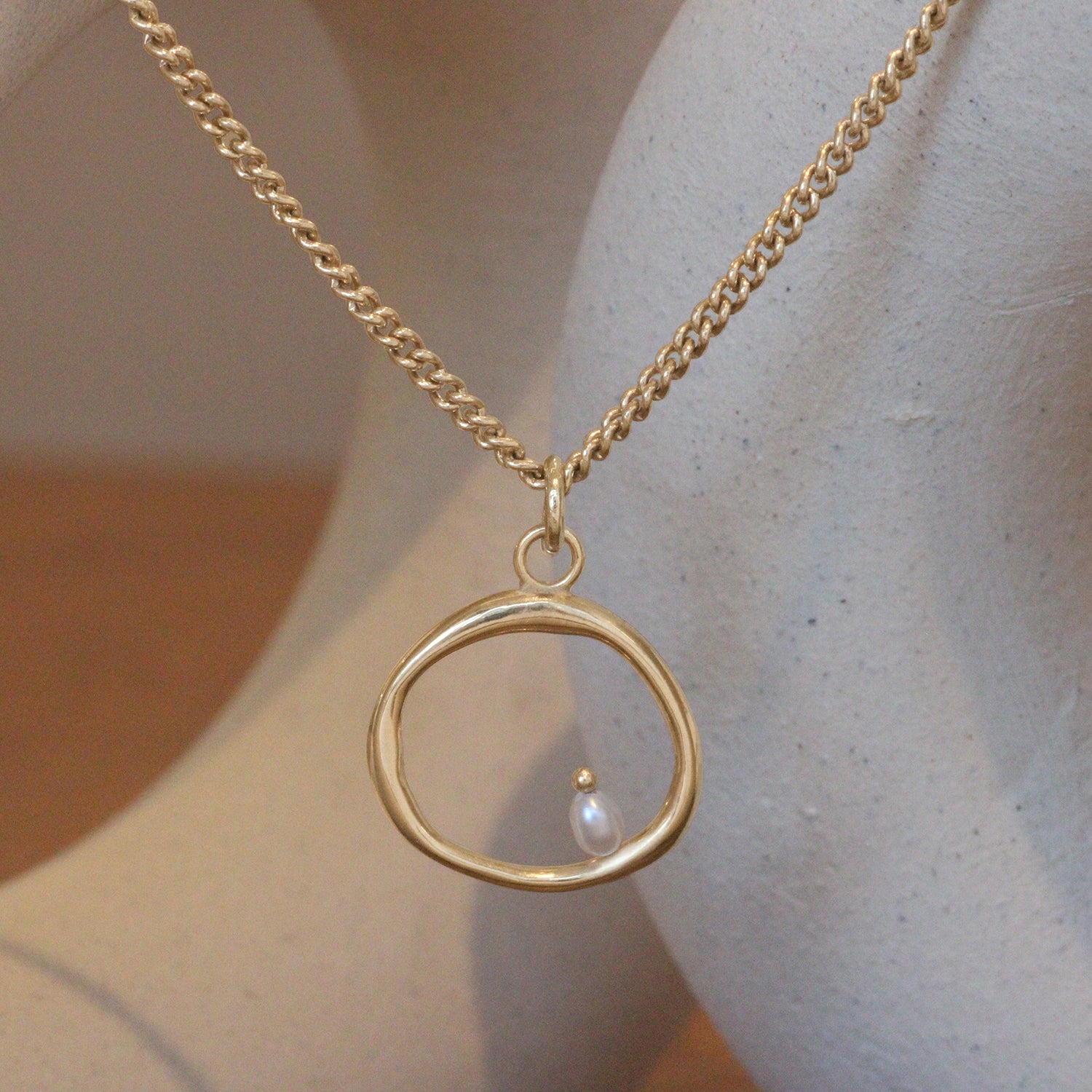 Lifestyle view of Amorphous Large Circle Bead Pearl Necklace / Cable Chain by Goldpoint Jewelry hanging with ceramics as a backdrop