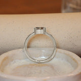 Lifestyle side profile view of Ash Ring Oval Sapphire 0.615ct by Goldpoint Jewelry sitting ona. ceramic with a blurred background