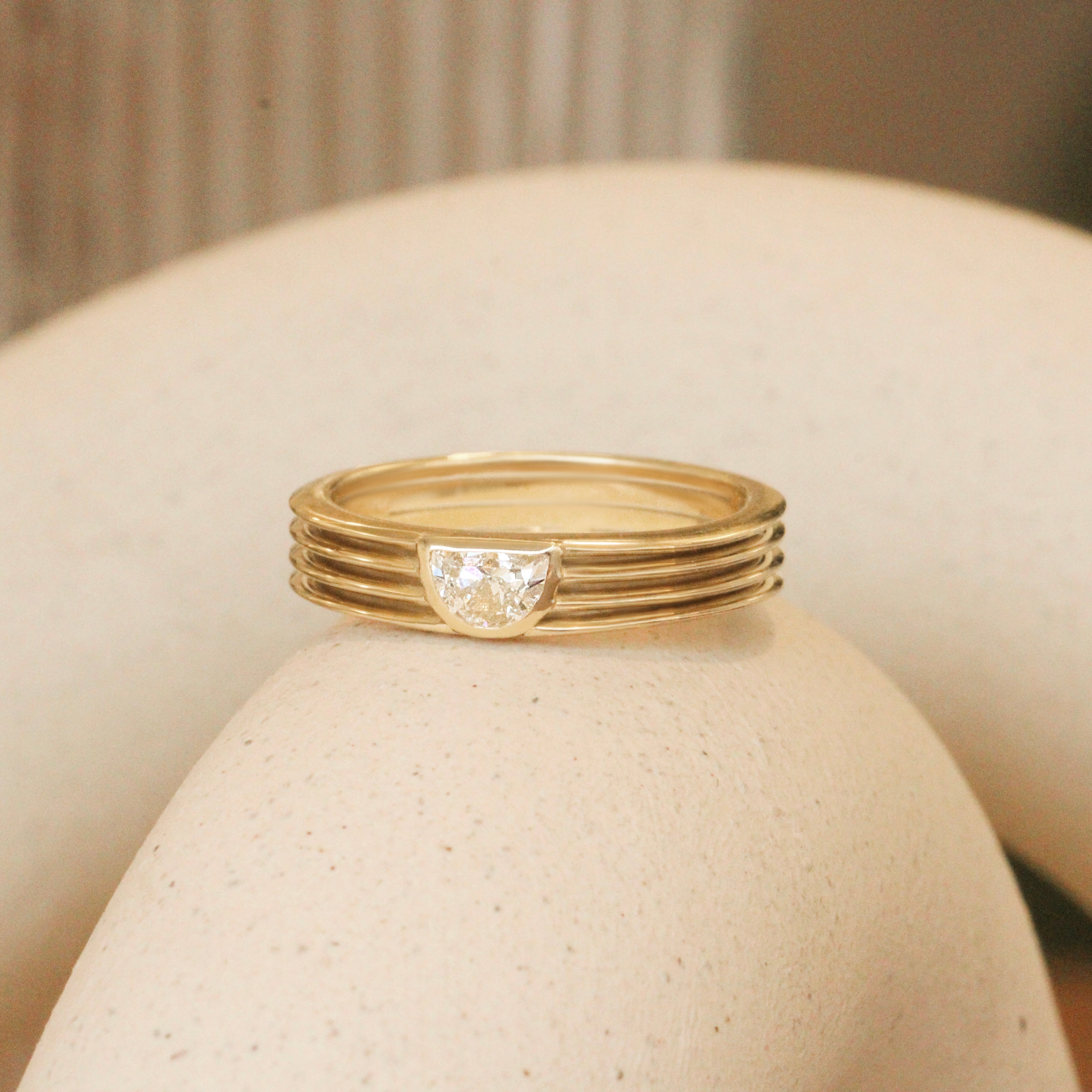 Lifestyle angled side view of Break of Day Ring / Half Moon Lab Diamond 0.25ct by Sandy Rubin on a ceramic with a blurred background