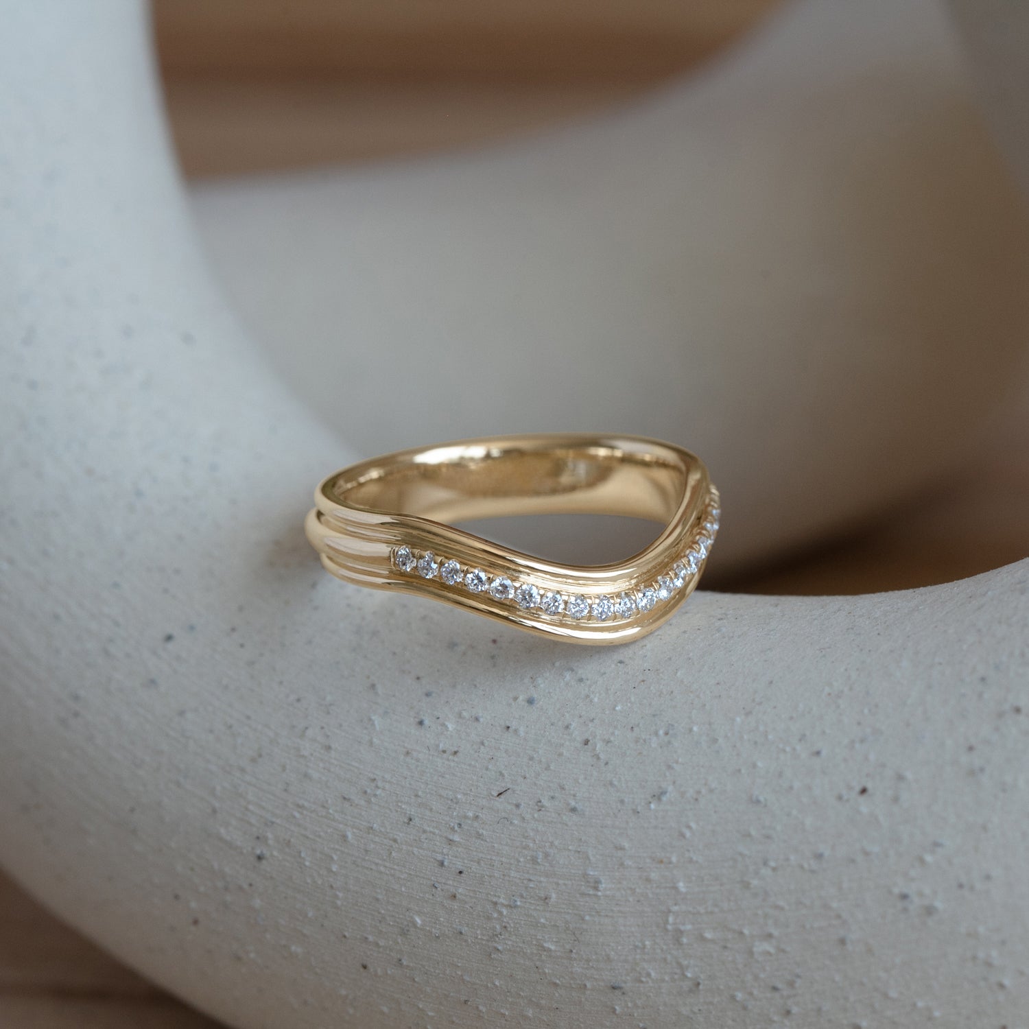 Lifestyle angled side view of Cornice Band Deep Curve / Pave Round Diamonds / in 14k Yellow Gold by Goldpoint Jewelry on a ceramic with blurred background