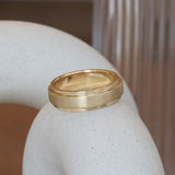 Lifestyle angled view of Cornice Flat Band Wide in 14k yellow gold by Goldpoint Jewelry on a ceramic with blurred background
