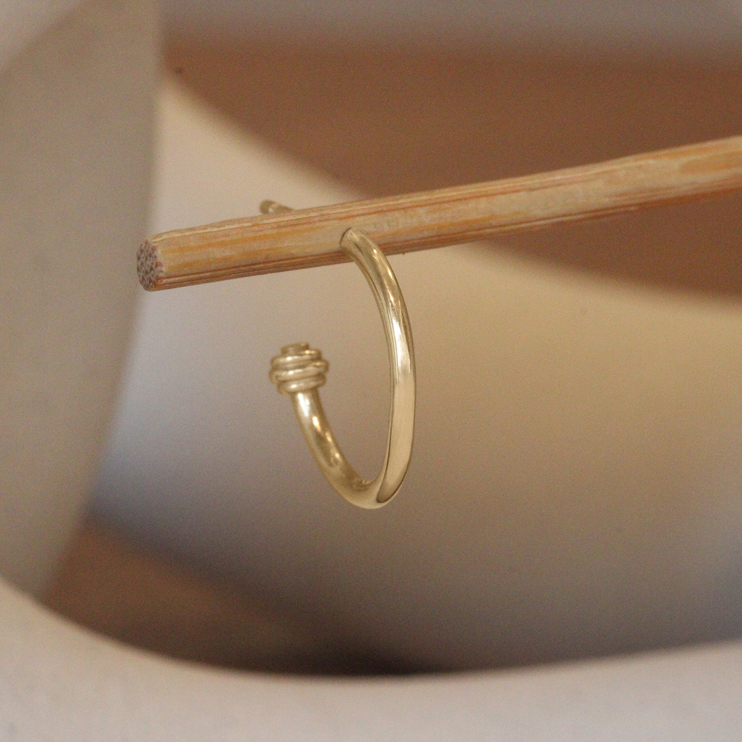 Lifestyle angled view of Cornice End Hoop / Medium by Goldpoint Jewelry on a wooden stand with a blurred background