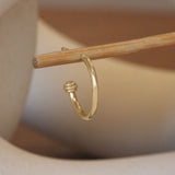 Lifestyle angled view of Cornice End Hoop / Medium by Goldpoint Jewelry on a wooden stand with a blurred background