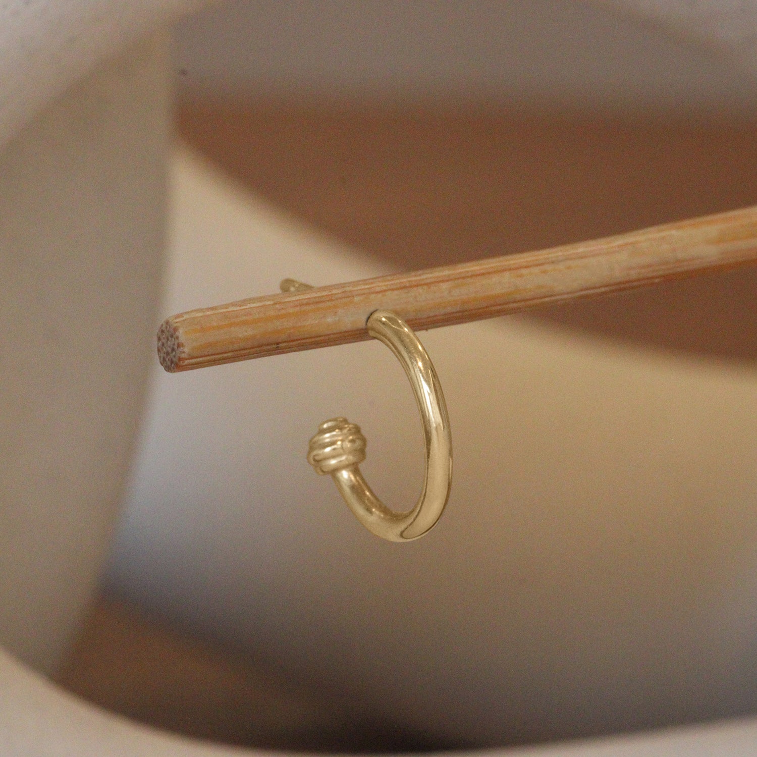 Lifestyle angled view of Cornice End Hoop / Small by Goldpoint Jewelry on a wooden stand with a blurred background