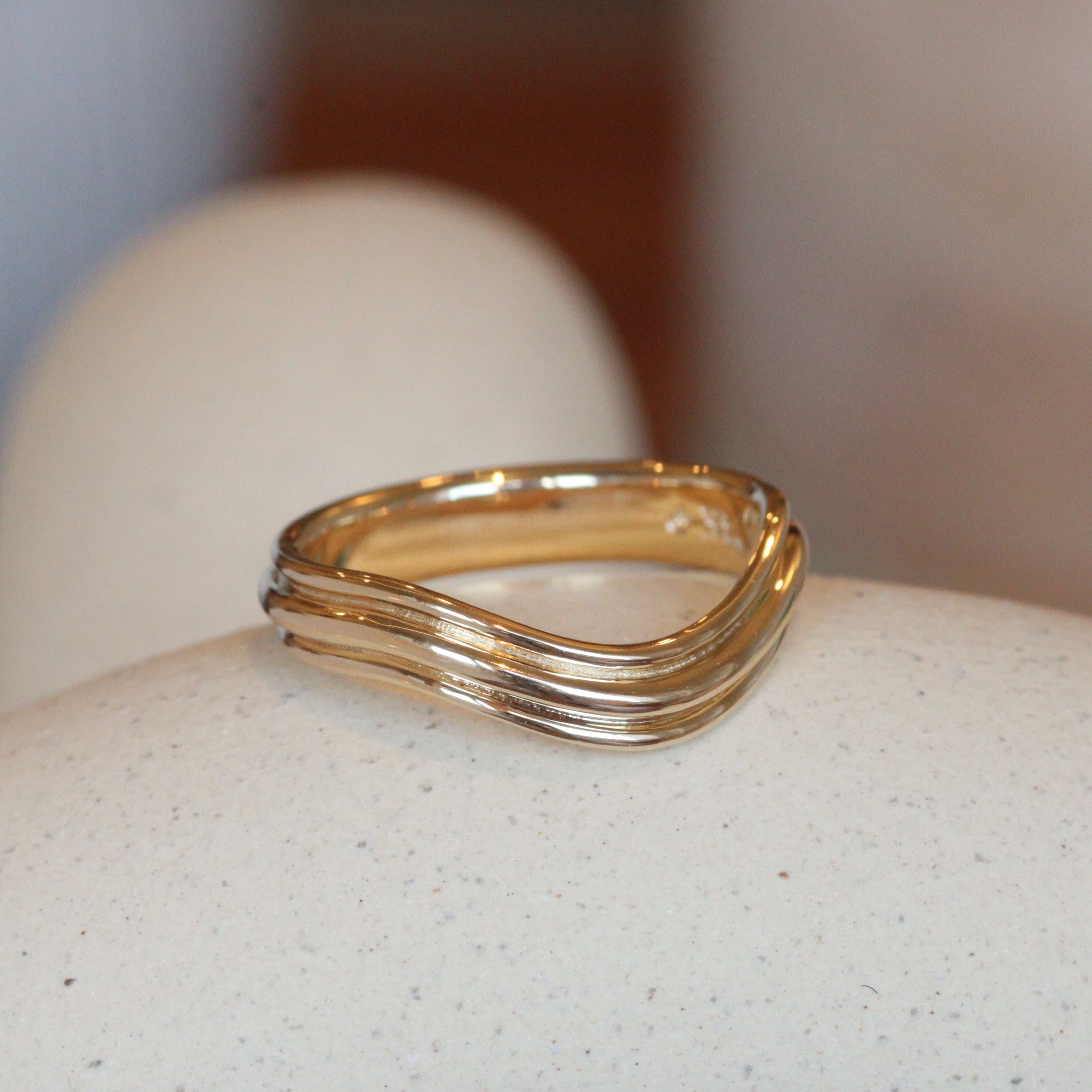 Lifestyle angled view of Cornice Band Deep Curve in 14k yellow gold by Goldpoint Jewelry on a ceramic