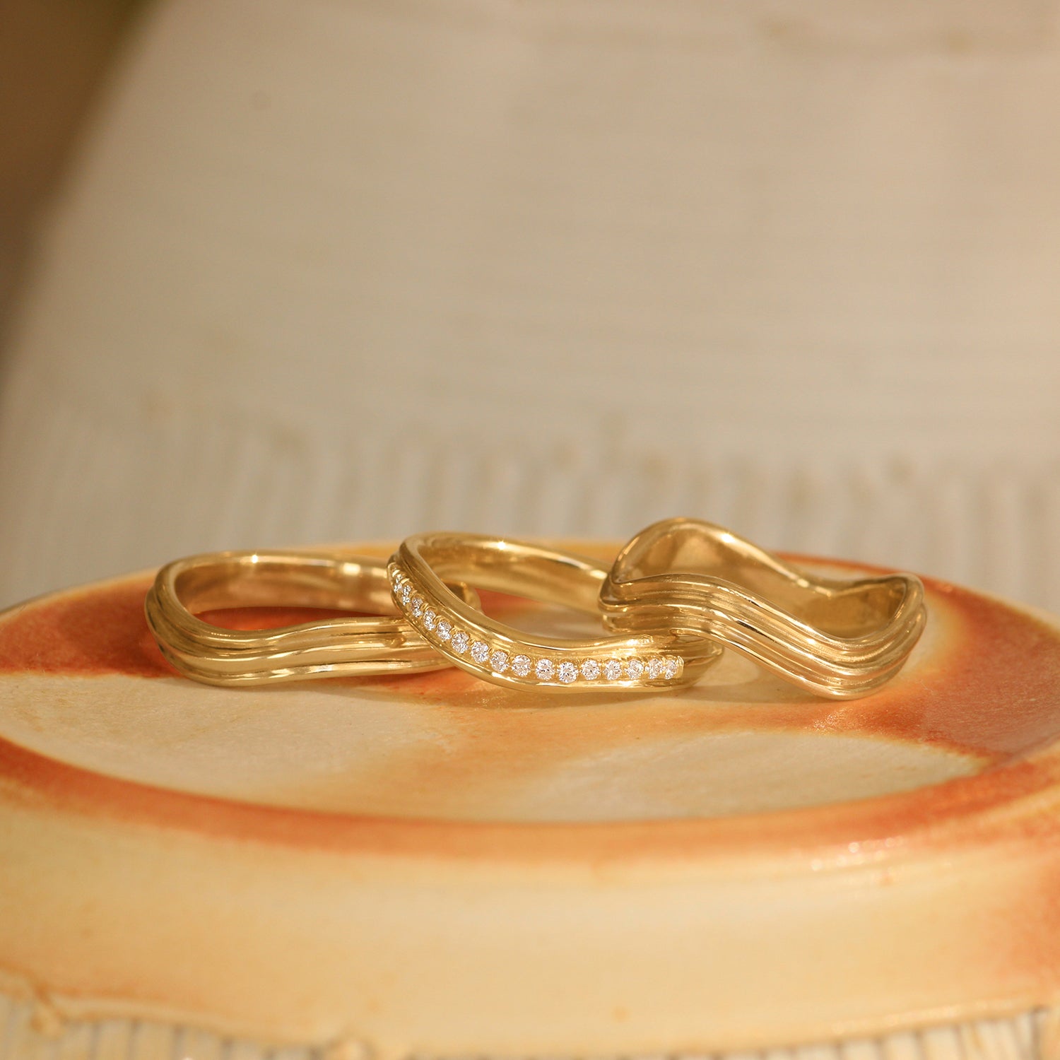 Lifestyle stacked view of Cornice Band Soft Curve Pave Round Diamonds in 18k yellow gold, Cornice Band Deep Curve in 14k yellow gold, and Cornice Band Soft Curve in 14k yellow gold
