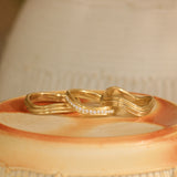 Lifestyle stacked view of Cornice Band Soft Curve Pave Round Diamonds in 18k yellow gold, Cornice Band Deep Curve in 14k yellow gold, and Cornice Band Soft Curve in 14k yellow gold
