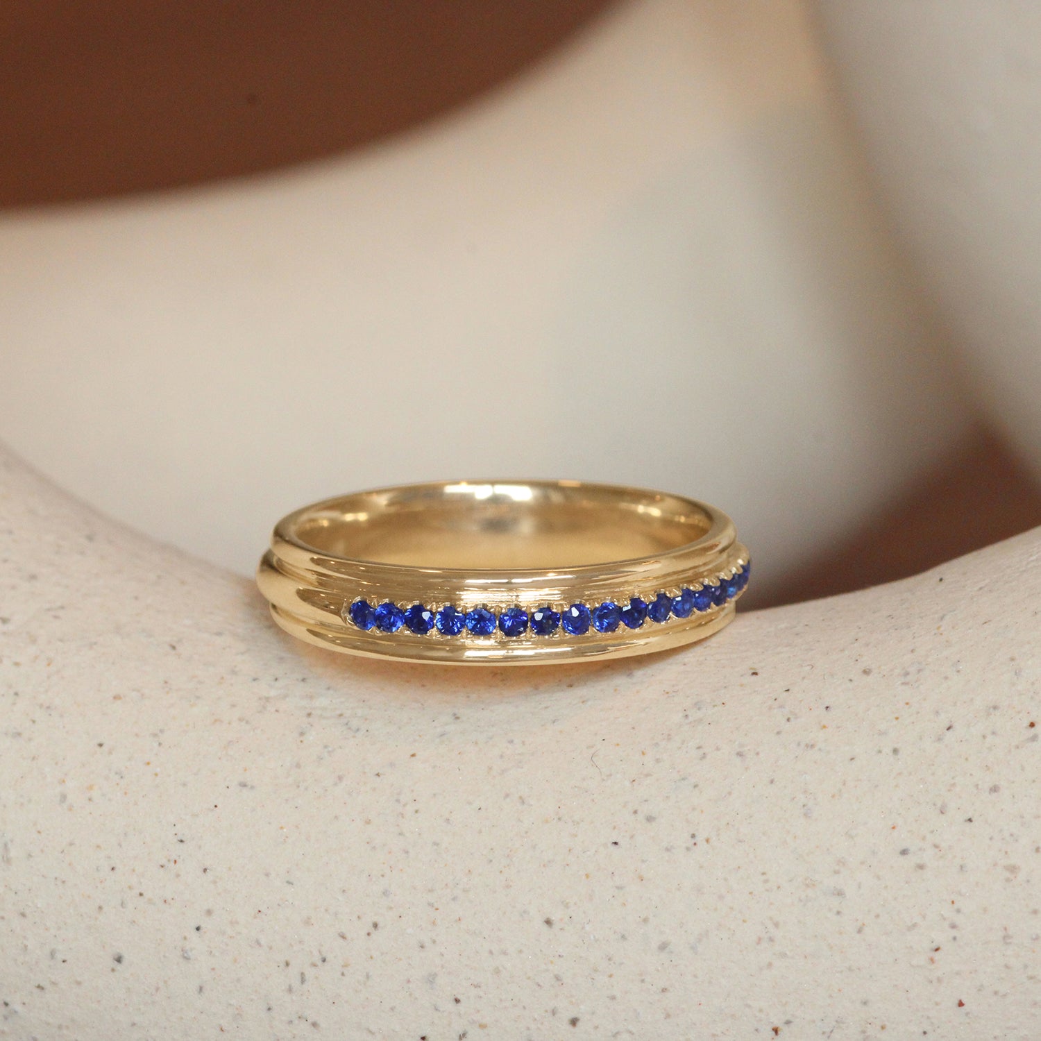 Lifestyle angled view of Cornice Band / Pave Round Sapphires in 14k Yellow Gold by Goldpoint Jewelry on a ceramic