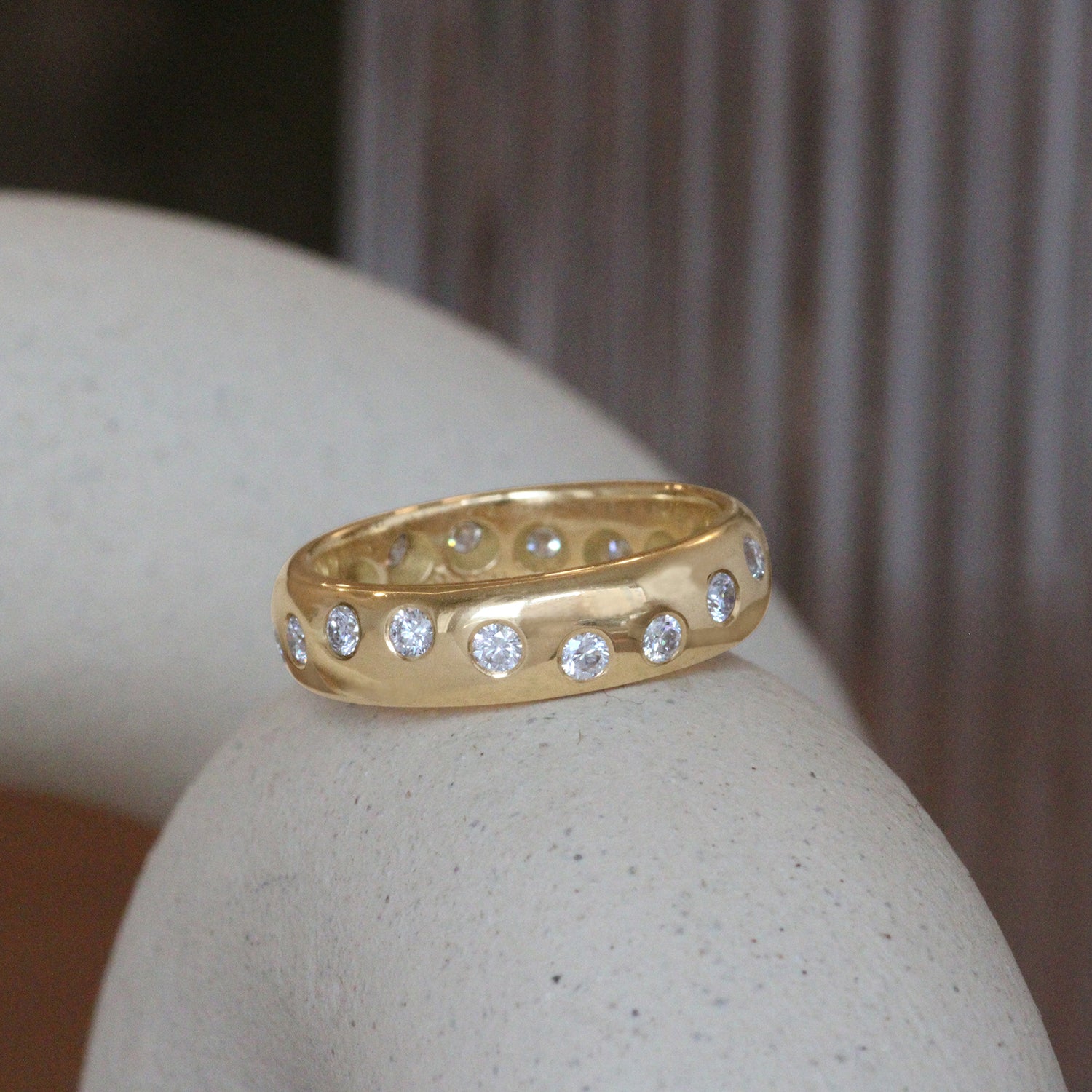 Lifestyle angled view of Dancing Band / Flush Round Natural Diamonds in 18k Yellow Gold by Goldpoint Jewelry on a ceramic with blurred background