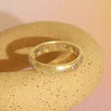 Lifestyle angled view of Dancing Band 5mm / Flush Princess Cut Lab Diamonds / in Yellow Gold ona ceramic with pink backdrop