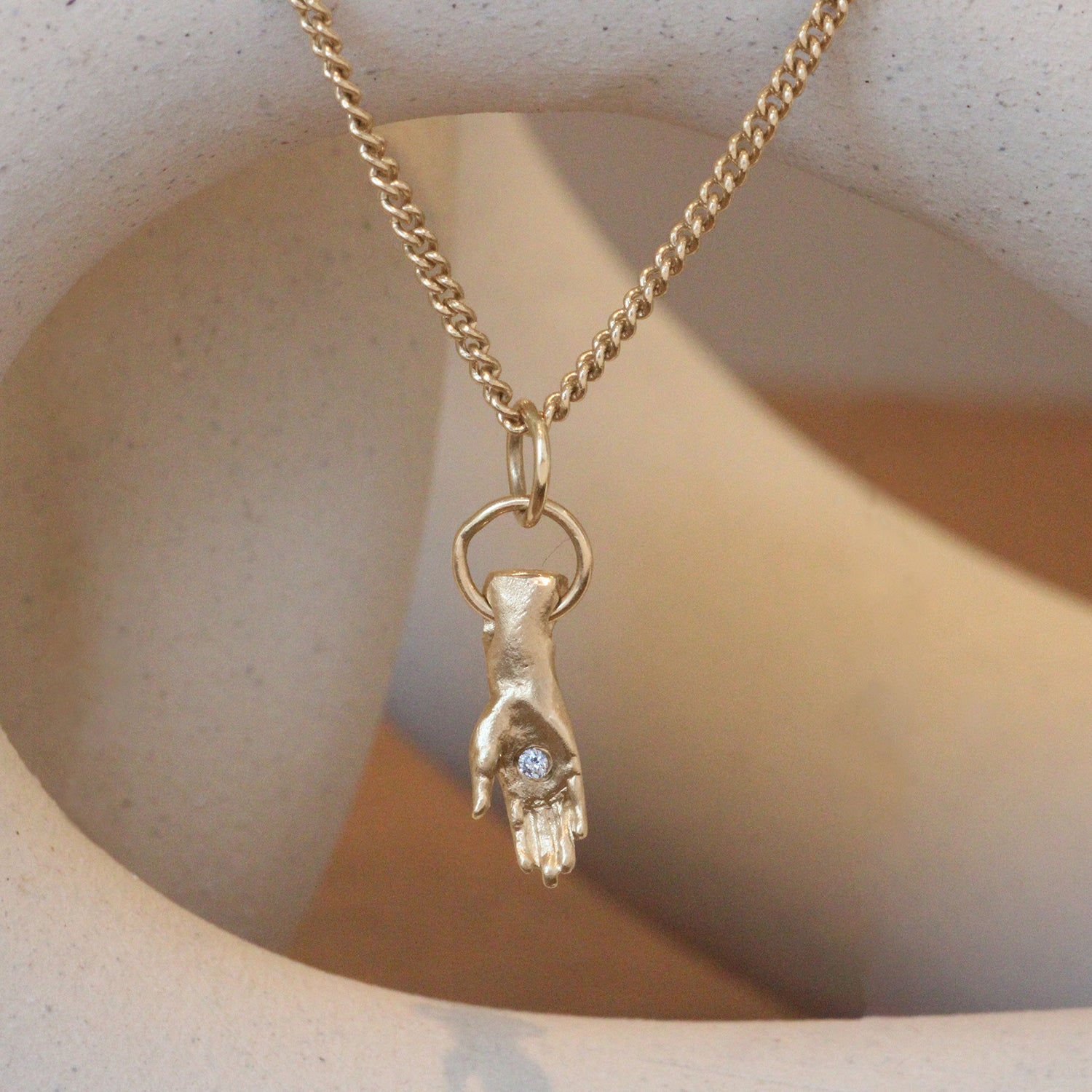 Lifestyle front view of Diamond Hand Charm / Round Natural Diamond by 12th House hanging with ceramics as a backdrop