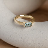Lifestyle angled view of Dobbin Ring Emerald Cut Sapphire 0.75ct by Goldpoint Jewelry on a ceramic with natural blurred backdrop