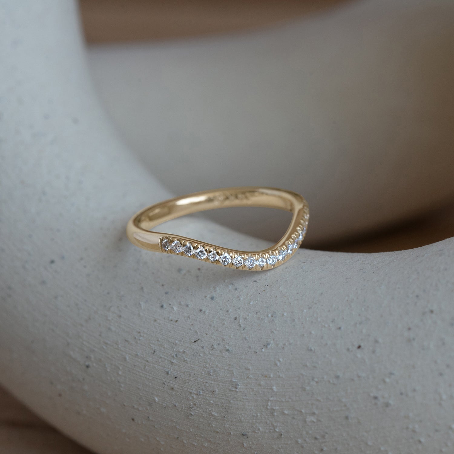 Lifestyle angled side view of Dome Band 2mm Deep Curve / Pave Round Lab Diamonds / in 14k Yellow Gold by Goldpoint Jewelry on a ceramic with blurred background