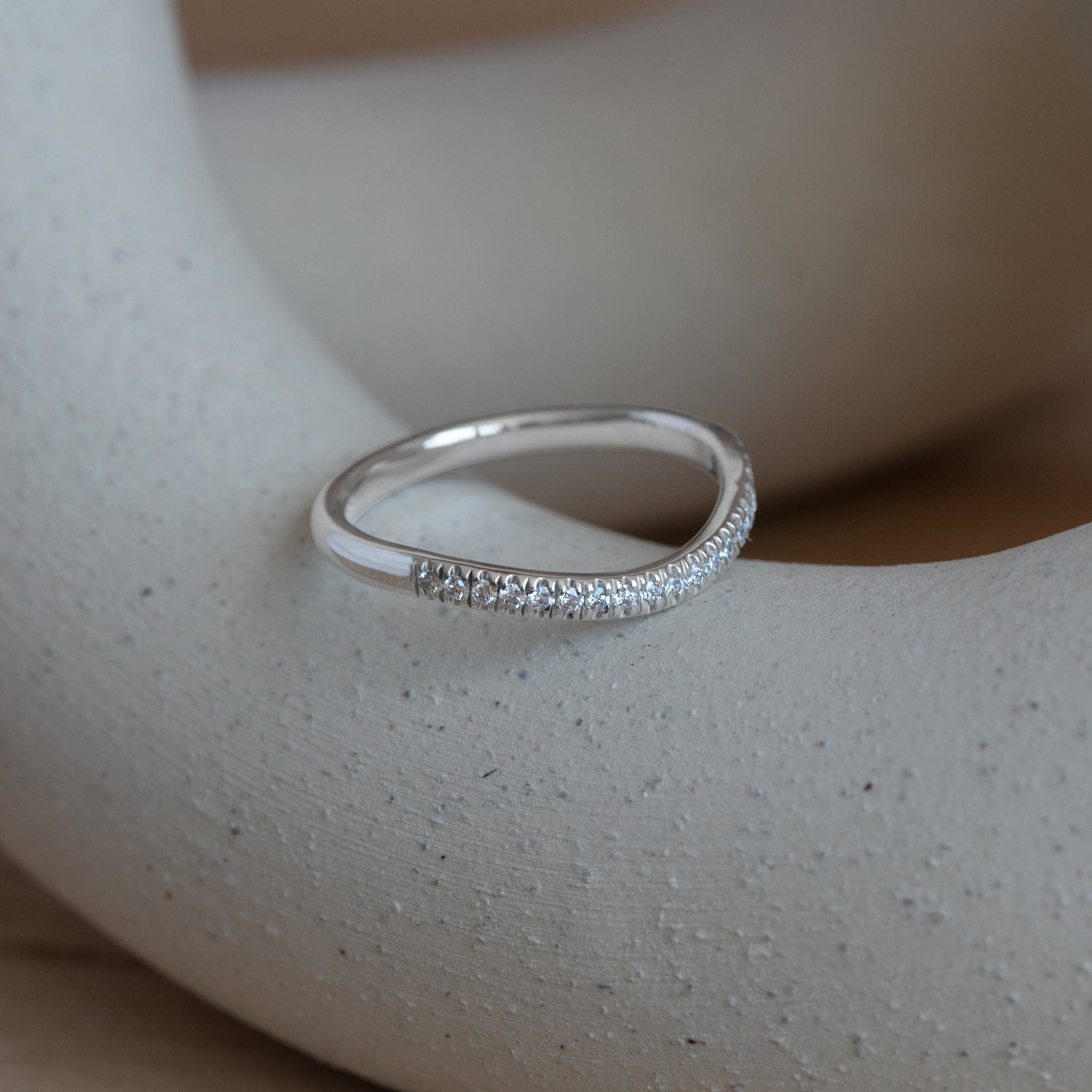 Lifestyle angled side view of Dome Band 2mm Soft Curve / Pave Round Diamonds / in Platinum by Goldpoint Jewelry on a ceramic with blurred background