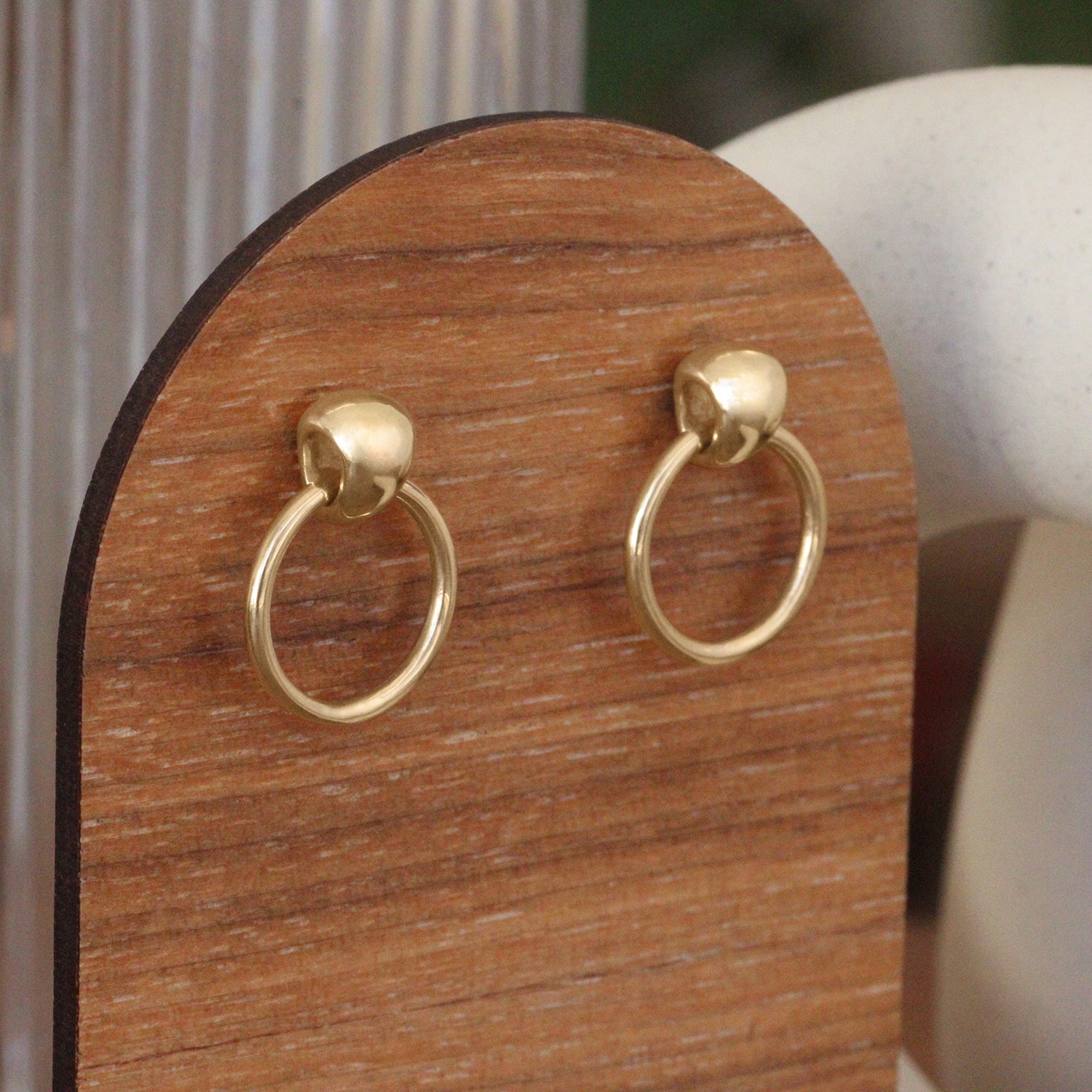 Lifestyle side angled view of Ruins Door Knocker Earring by Goldpoint Jewelry on a wood stand