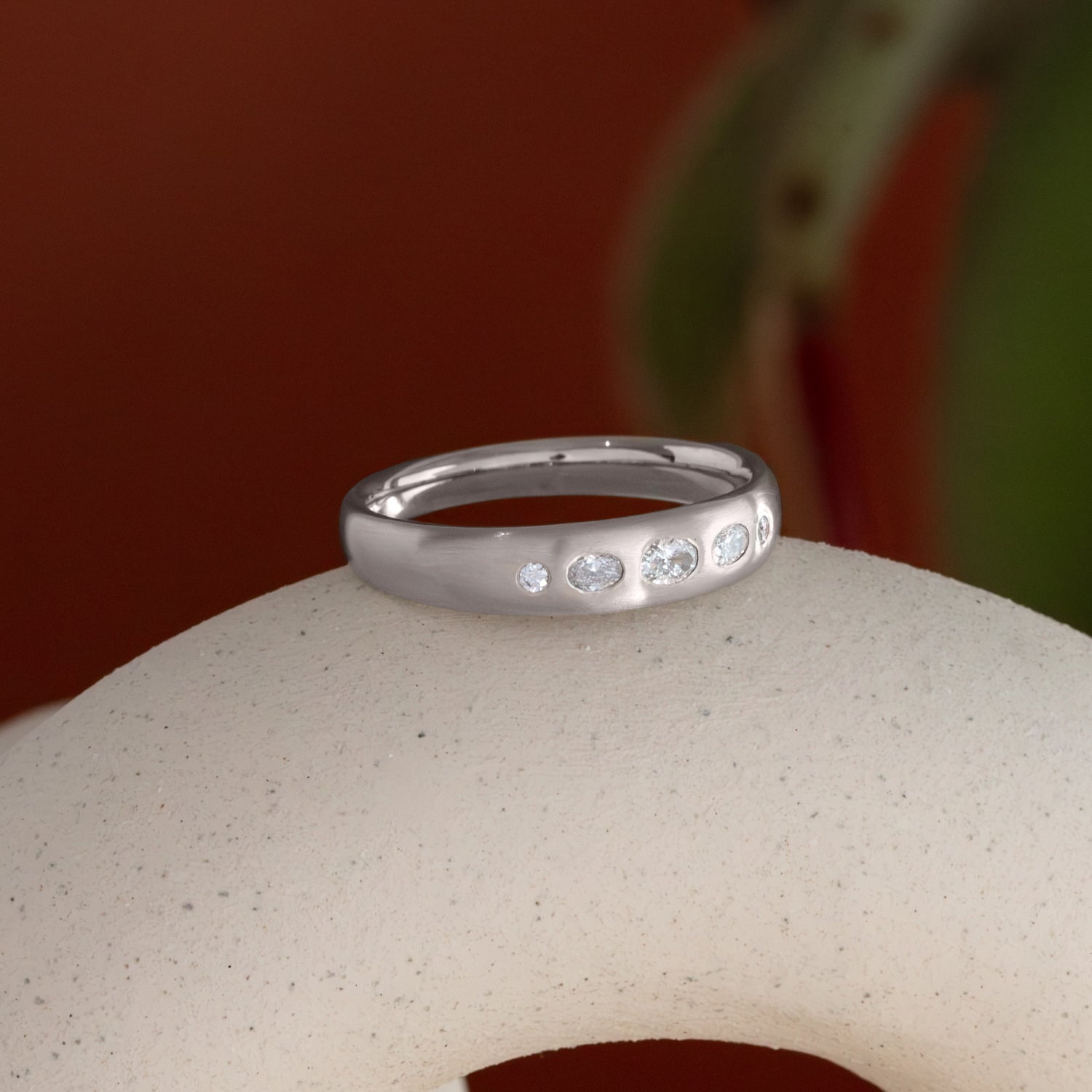 Lifestyle angled side view of Ellipse Band 5mm / Flush Oval Lab Diamond / in 14k White Gold by Goldpoint Jewelry on a ceramic with blurred background