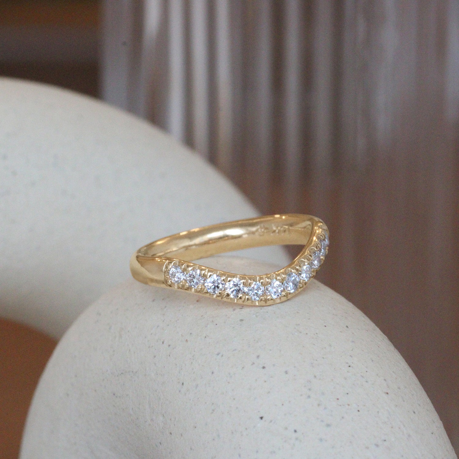 Lifestyle angled side view of Ellipse Band Deep Curve / Pave Round Lab Diamonds / in 14k Yellow Gold by Goldpoint Jewelry on a ceramic with a blurred background