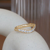 Lifestyle angled side view of Ellipse Band Deep Curve / Pave Round Lab Diamonds / in 14k Yellow Gold by Goldpoint Jewelry on a ceramic with a blurred background