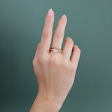 Model wears Flat Band Deep Curve in 14k yellow gold stacked with an engagement ring by Goldpoint Jewelry on their middle finger with a teal background