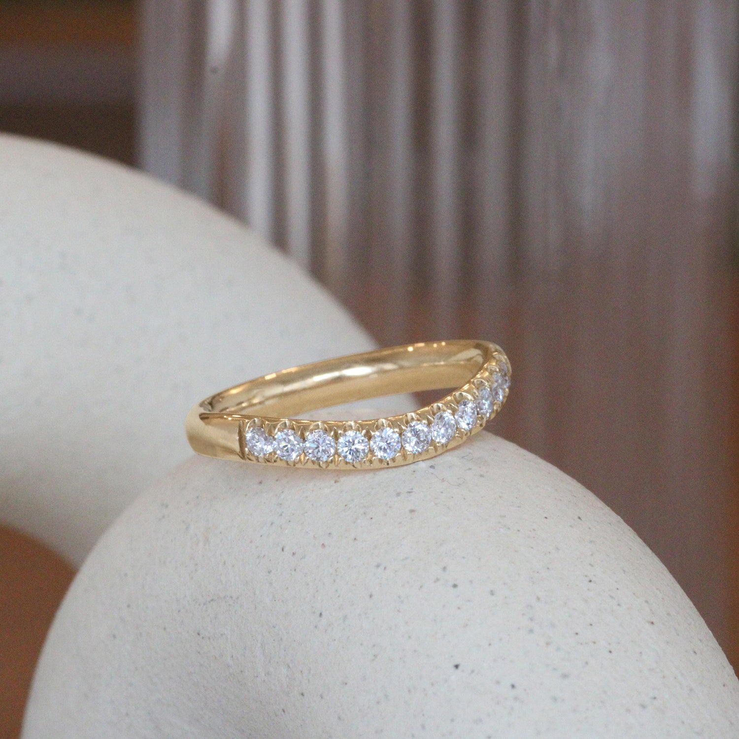 Lifestyle angled view of Ellipse Band Soft Curve Pave / Round Lab Diamonds / in 14k Yellow Gold by Goldpoint Jewelry on a ceramic with blurred background