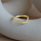 Lifestyle angled view of Flat Band 2mm Deep Curve / in 18k Yellow Gold by Goldpoint Jewelry on a ceramic with blurred background