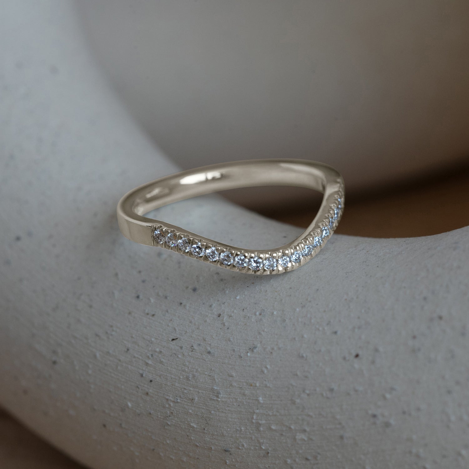 Lifestyle side profile view of Flat Band 2mm Deep Curve / Pave Round Diamonds / in 14k White Gold by Goldpoint Jewelry on a ceramic with blurred background