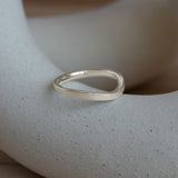 Lifestyle angled side view of Flat Band 2mm Soft Curve / in 14k White Gold by Goldpoint Jewelry on a ceramic with blurred background