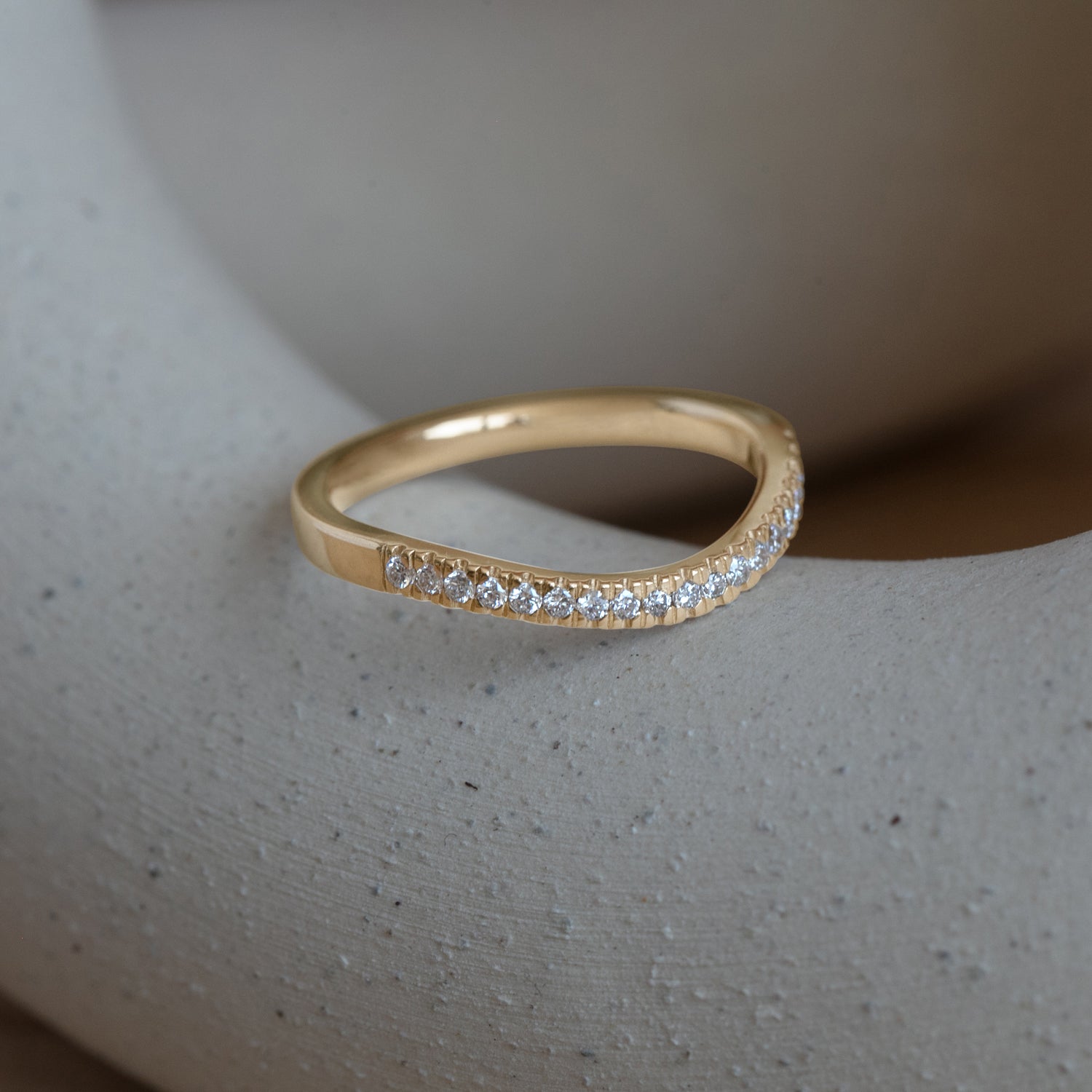Lifestyle angled side view of Flat Band 2mm Soft Curve / Pave Round Diamonds / in 14k Yellow Gold by Goldpoint Jewelry on a ceramic with a blurred background
