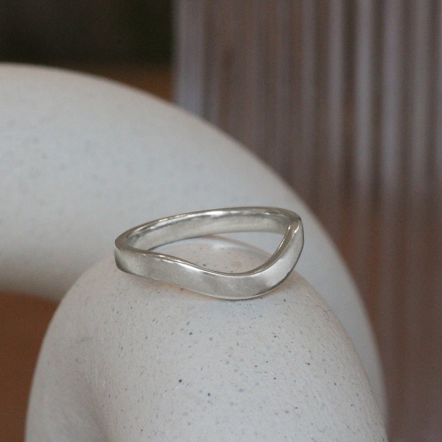 Lifestyle angled side view of Flat Wide Band Deep Curve in Platinum by Goldpoint Jewelry on a ceramic with blurred background