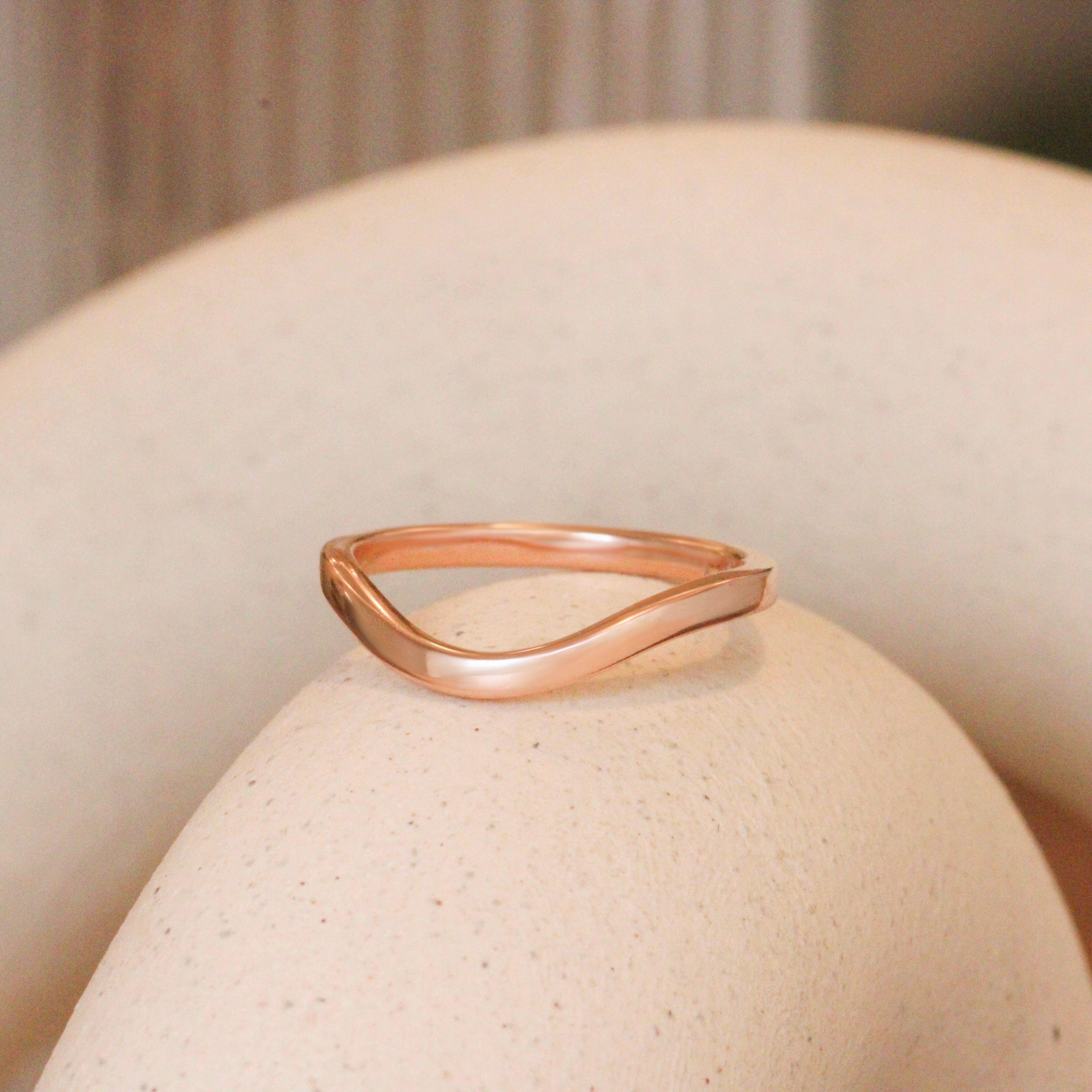 Lifestyle angled view of Flat Band 2mm Deep Curve / in 14k Rose Gold by Goldpoint Jewelry on a ceramic with blurred background