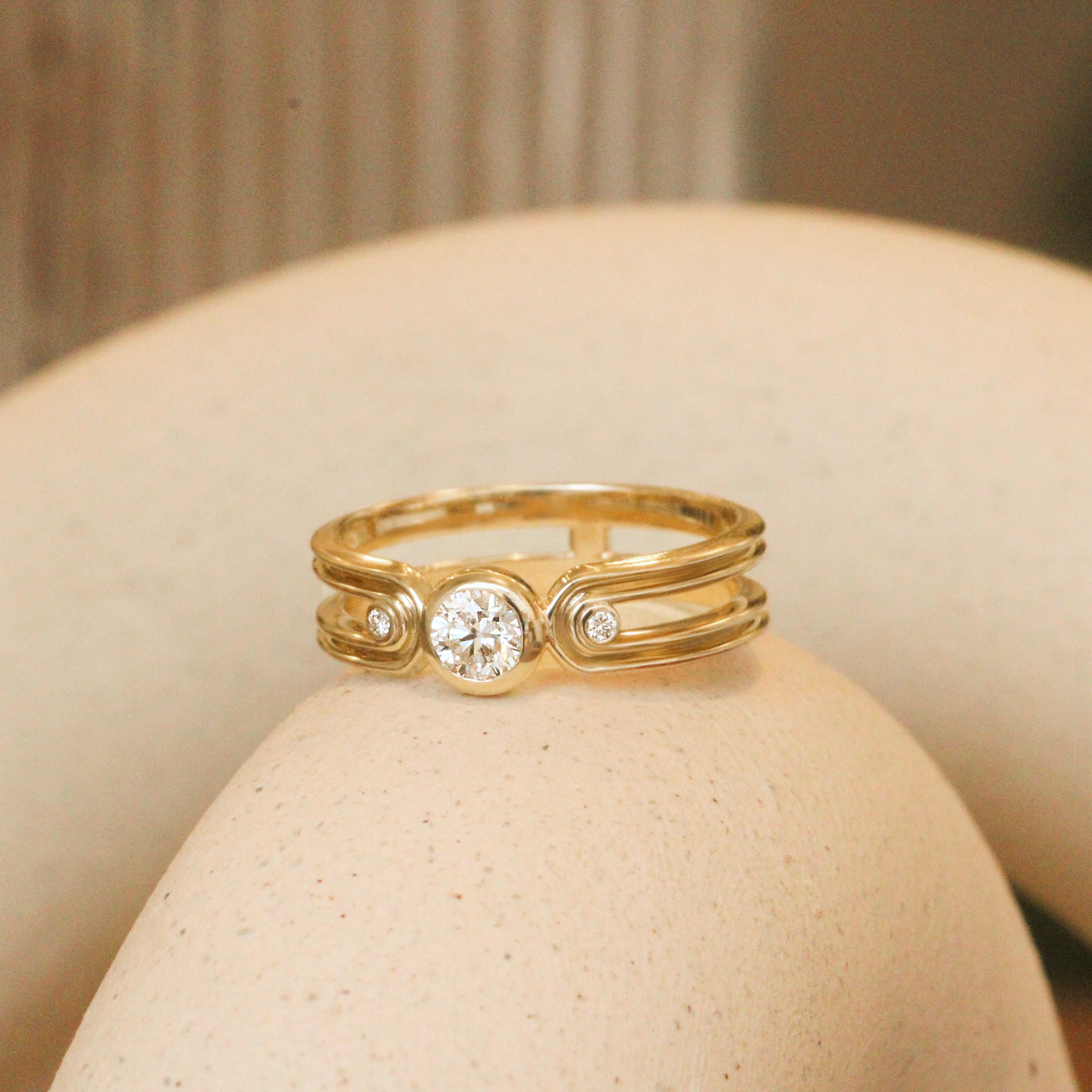 Lifestyle angled side angled view of Gravitational Pull Ring / Round Natural Diamond 0.25ct by Sandy Rubin on a ceramic with blurred background