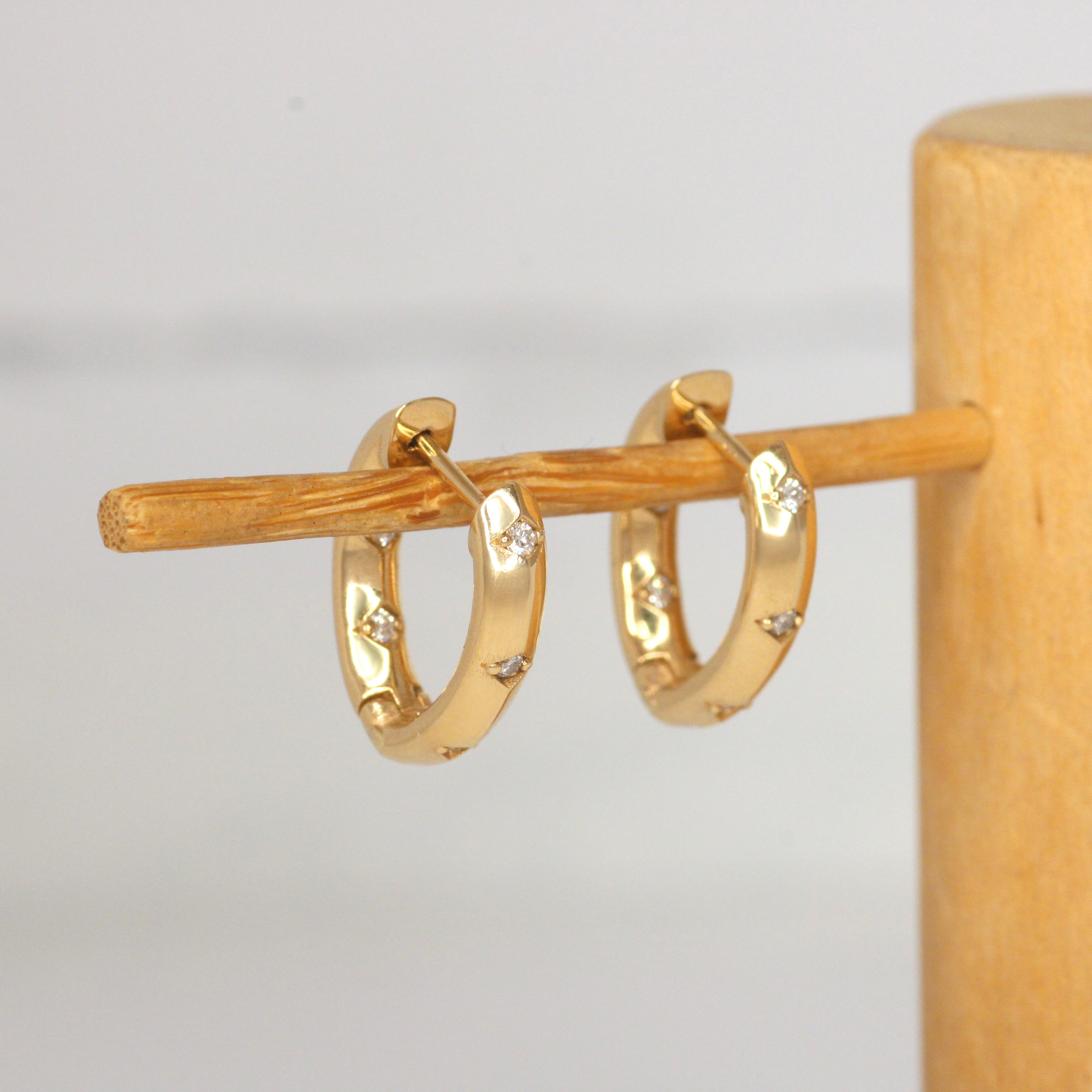 Lifestyle angled view of Hilma Hoops / Natural Round Diamonds by 12th House on a wooden stand with blurred background