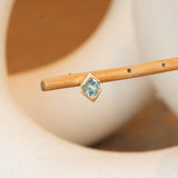 Lifestyle angled side view of Horus Earring / Round Aquamarine by Goldpoint Jewelry on a wooden stand with blurred background