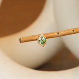 Lifestyle angled view of Horus Earring / Round Peridot by Goldpoint Jewelry on a wooden stand with blurred background