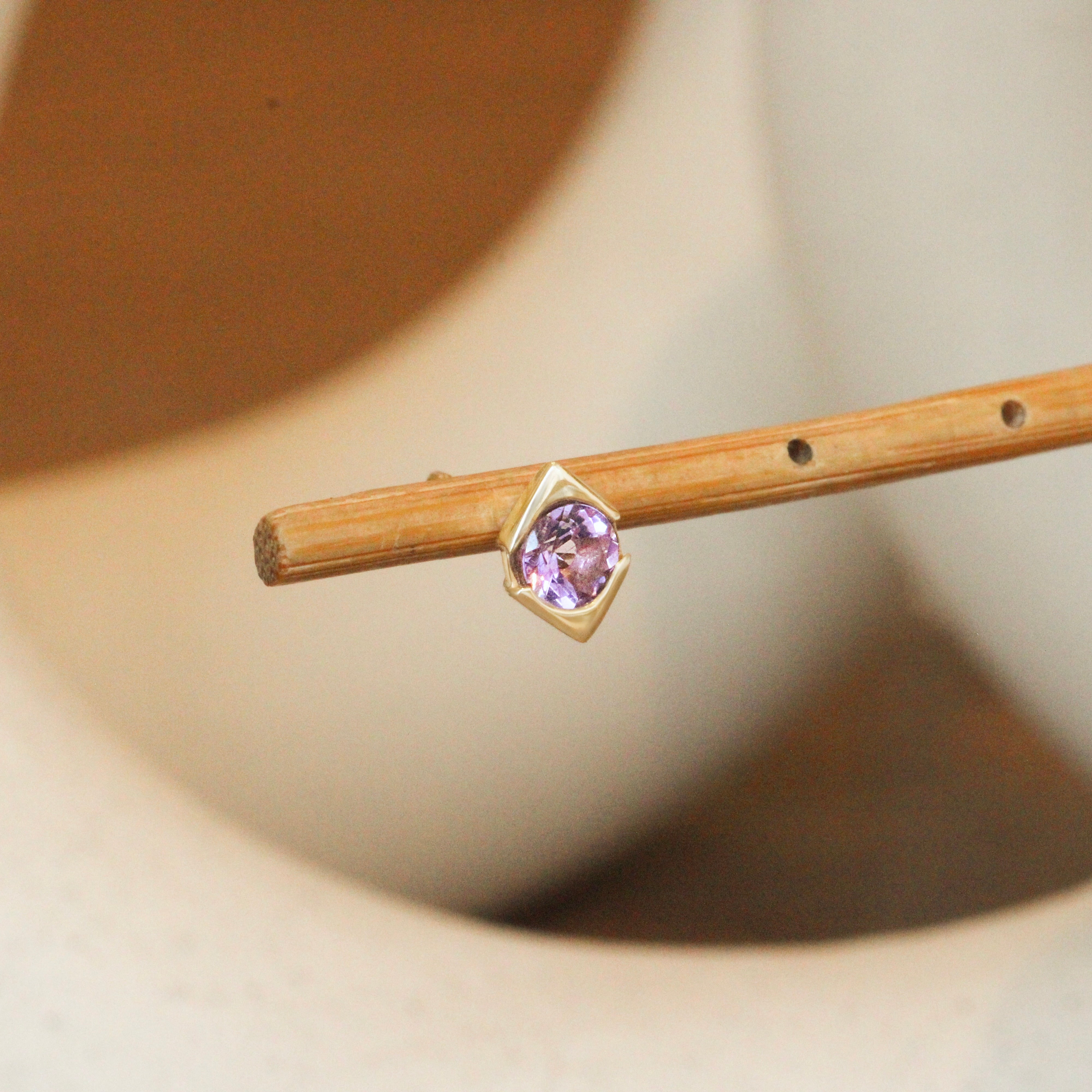 Lifestyle angled side view of Horus Earring / Round Amethyst by Goldpoint Jewelry on a wooden stand with blurred background