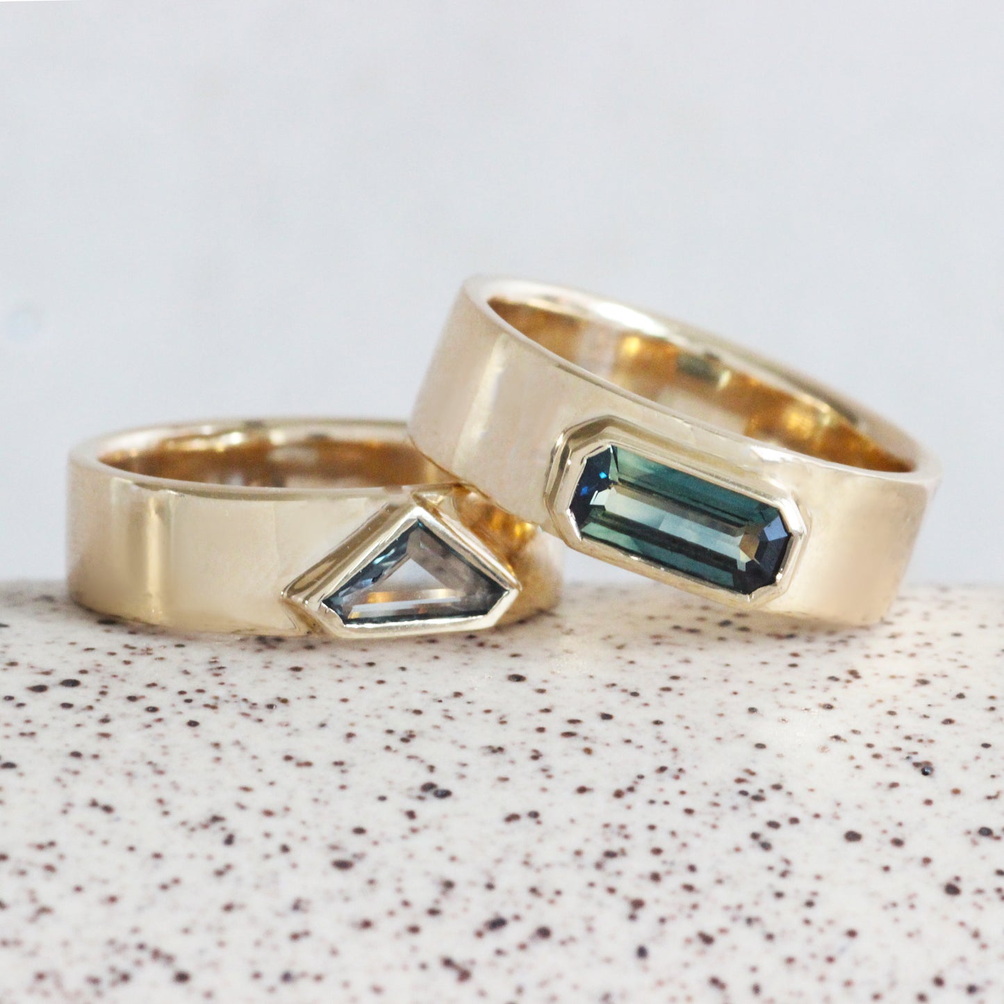 Front view of Horizon Band / Bicolor Blue Yellow Emerald Cut Sapphire leaning on Horizon Band / Portrait Cut Grey-Blue Sapphire