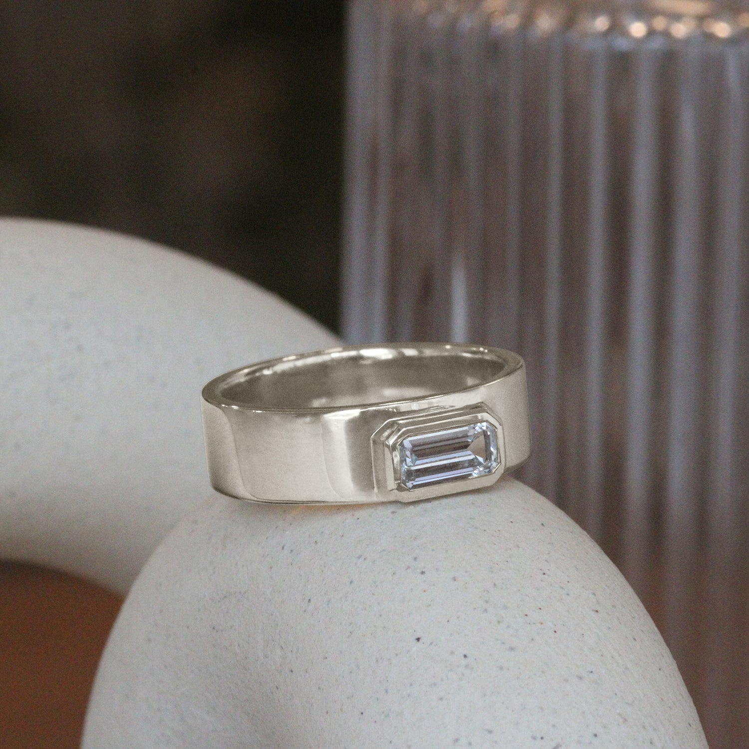 Lifestyle angled side view of Kingsland Ring Emerald Cut Sapphire 0.85ct in 14k white gold by Goldpoint Jewelry on a ceramic with blurred background