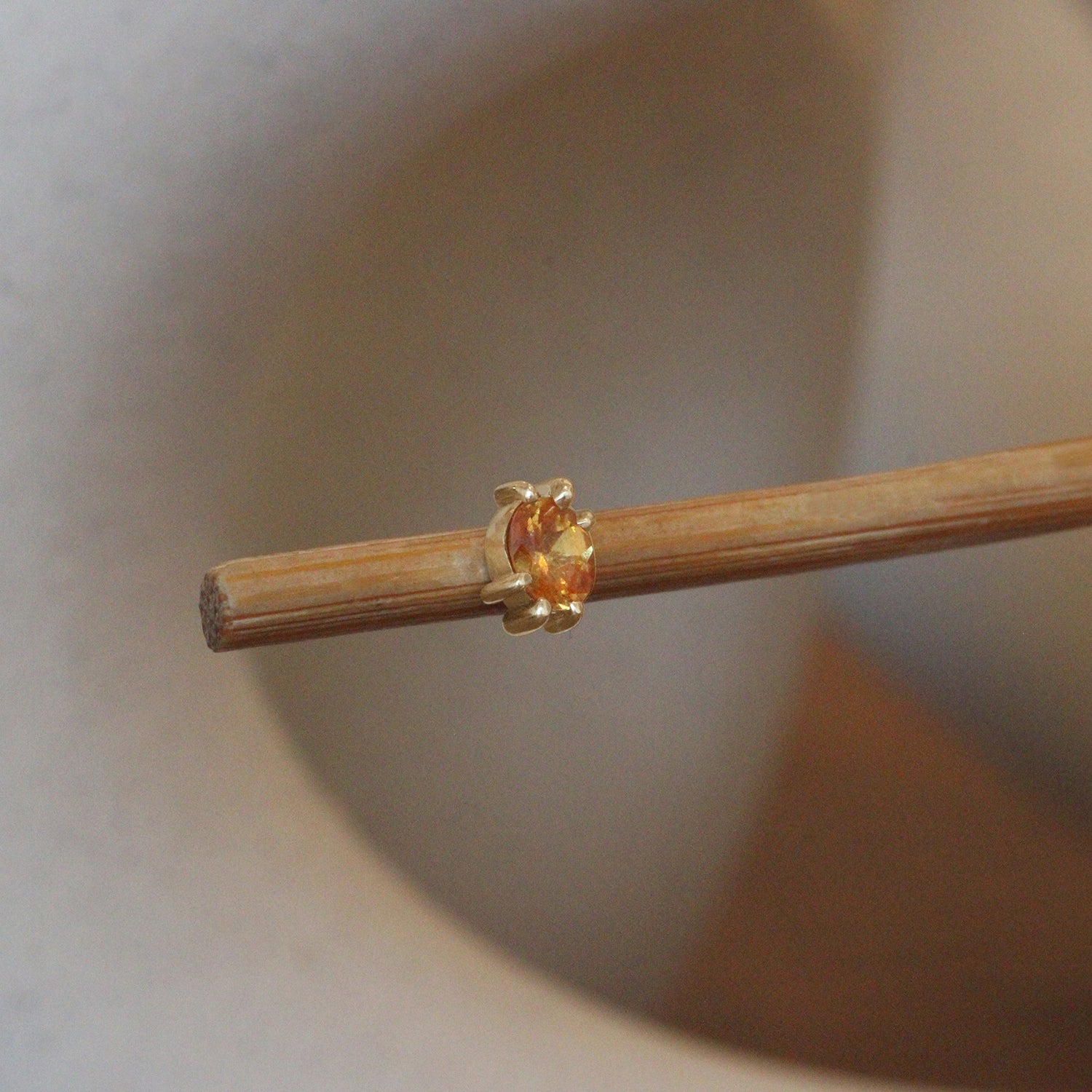 Lifestyle angled view of Miro Earring / Oval Orange Spessartite Garnet in 14k yellow gold by Goldpoint Jewelry on a wooden stand with a blurred background