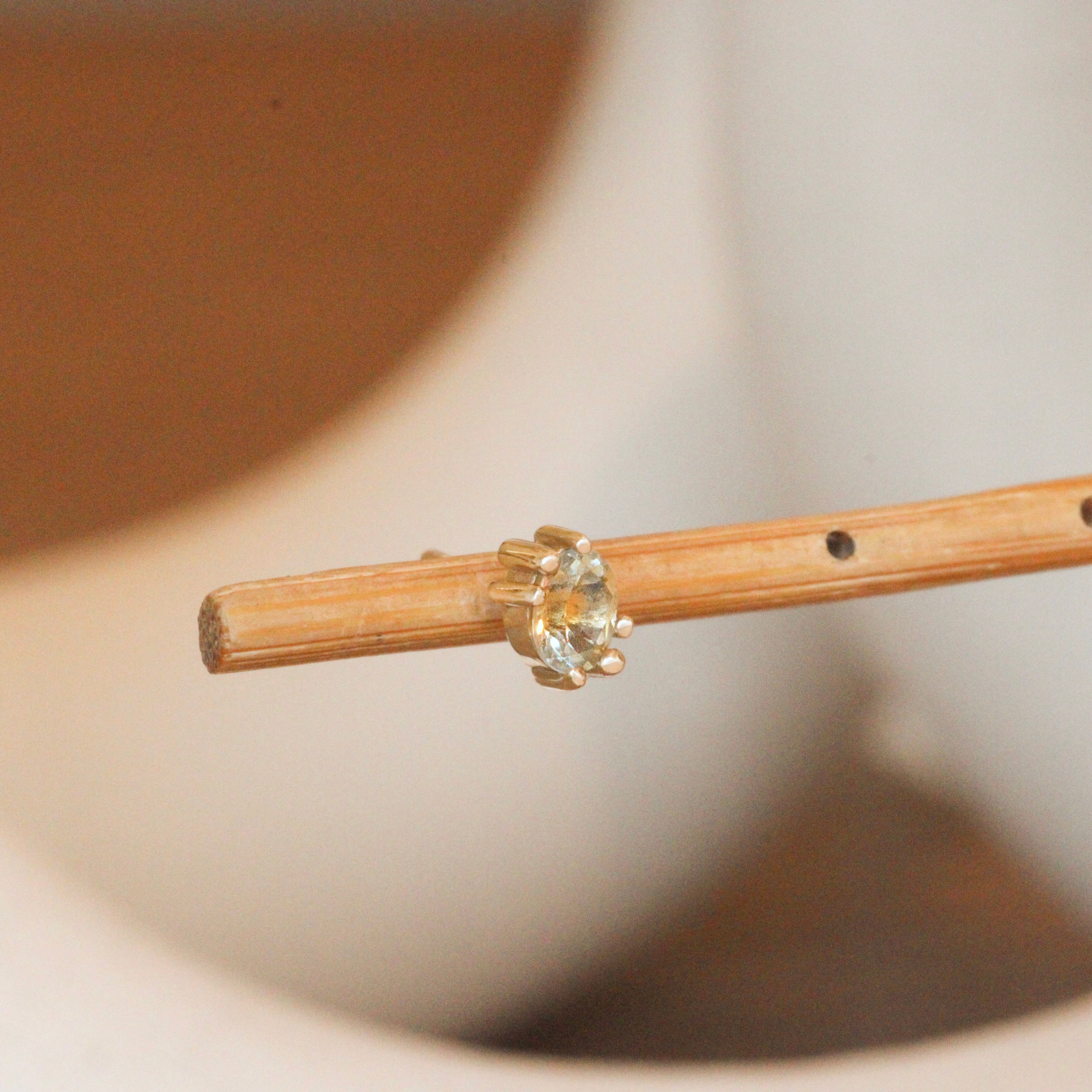 Angled view of Miro Earring / Oval Yellow Kaleidoscope Sapphire by Goldpoint Jewelry on a wooden stand with a blurred background